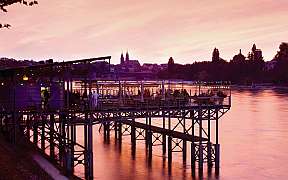 Ein Steg mit Restaurantbeleuchtung am Fluss bei Sonnenuntergang.