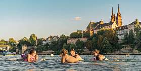 Group of people swimming and relaxing in a river with historic buildings in background