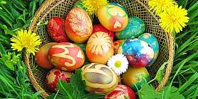 Un panier avec des œufs de Pâques colorés et des fleurs jaunes dans l'herbe.