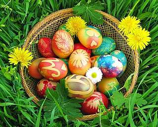 Ein Korb mit kunstvoll gefärbten Ostereiern und Blumen im Gras.