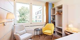 Helles Hotelzimmer mit Doppelbett, Schreibtisch und Fernseher.