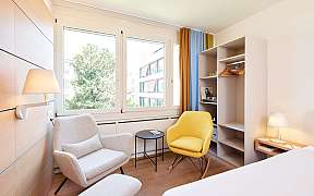 Helles Hotelzimmer mit Doppelbett, Schreibtisch und Fernseher.