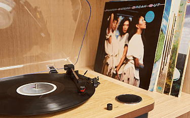 Ein Plattenspieler mit einer schwarzen Schallplatte und mehreren Schallplatten im Hintergrund.