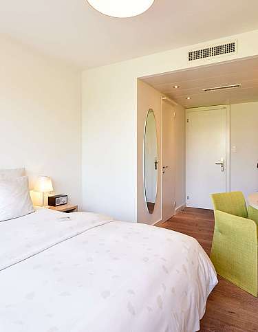 Modernes Hotelzimmer mit zwei Betten, Schreibtisch und Fernseher.