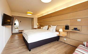 Helles Hotelzimmer mit Doppelbett, Fernseher und Schreibtisch.