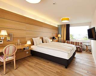 Helles Hotelzimmer mit Doppelbett, Schreibtisch und Fernseher.