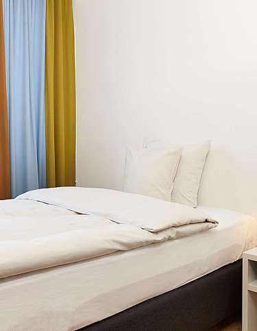 Gemütliches Schlafzimmer mit Bett, Nachttisch und bunten Vorhängen.