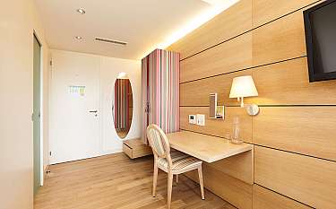 A bright hotel room with wooden paneling and a desk.