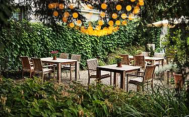 Ein ruhiger Garten mit Holztischen und Stühlen, umgeben von Pflanzen.