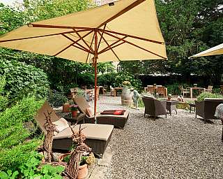 Ein einladender Garten mit Liegen und Tischen unter Sonnenschirmen.