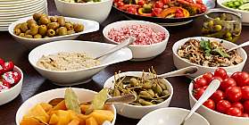 Bunte Auswahl an Vorspeisen in weißen Schalen auf einem Tisch.