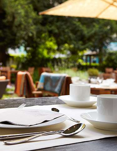 Tischgedeck mit Tassen und Besteck in einem Gartenrestaurant.