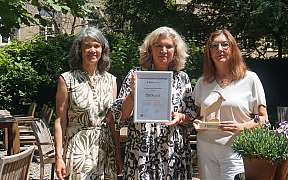 Three women holding a sustainability certificate and an award.
