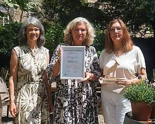 Three women presenting a sustainability certificate and an award outdoors.