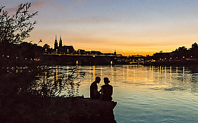 Silhouette of a couple by the water with a city view in the background.